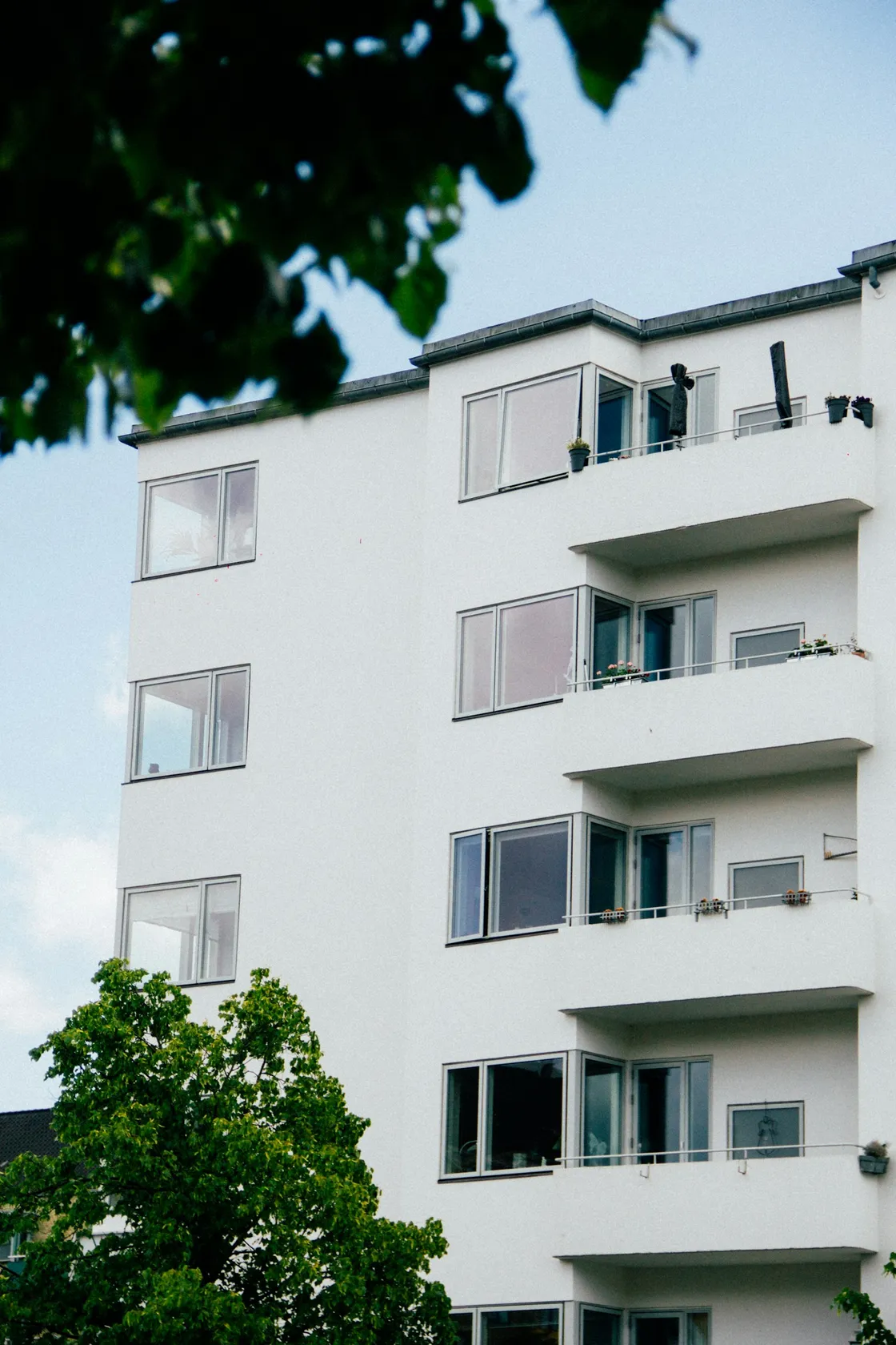 Edificio residencial blanco con balcones, entre árboles y bajo un cielo despejado